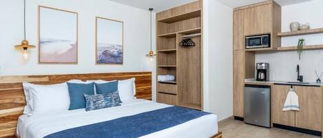 Une chambre comprenant un lit, des tables de chevet, une armoire en bois, une kitchenette équipée d’un four à micro-ondes et d’une machine à café.