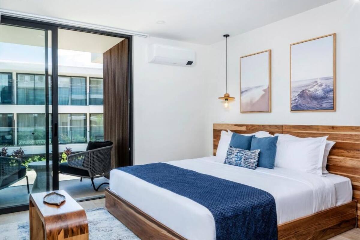 A modern hotel room with a large bed, a view through a sliding door to an outdoor area, and two framed pictures on the wall.