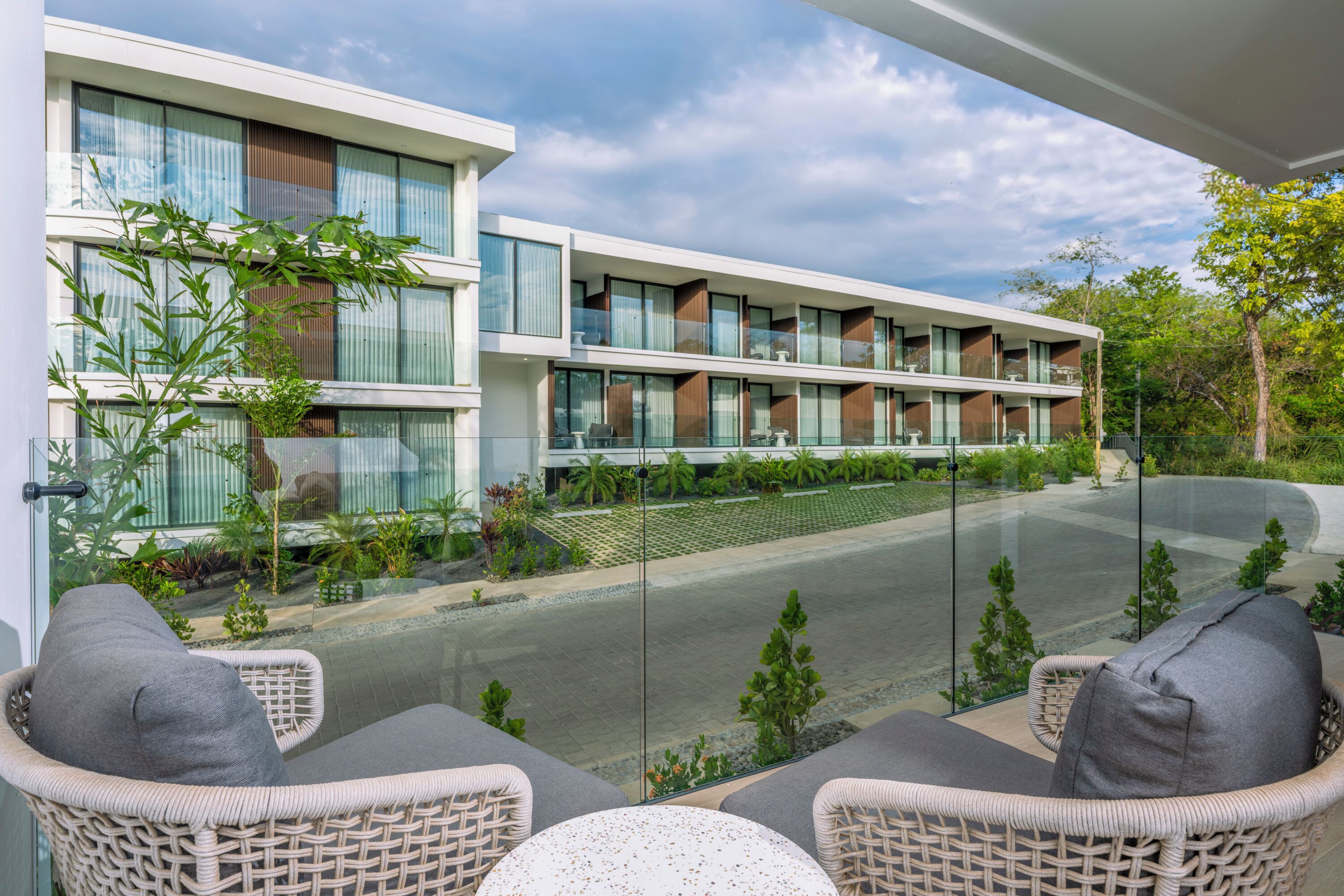Un hôtel moderne doté d’un balcon en verre, de meubles en osier et offrant une vue sur la rue.