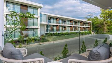 Un hôtel moderne doté d’un balcon en verre, de meubles en osier et offrant une vue sur la rue.