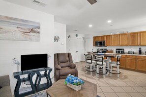 A living room with a flat-screen TV, a brown leather chair, and a table with a blue floral arrangement. - Gulf Breeze Coastal Cottage*Beach* Shopping*Dining (Gulf Breeze)