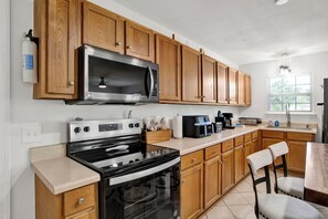 A kitchen with wooden cabinets, a stainless steel microwave, a stove, and a coffee maker. - Gulf Breeze Coastal Cottage*Beach* Shopping*Dining (Gulf Breeze)
