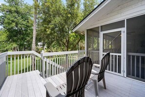 A covered outdoor deck with a white railing, two chairs, and a table. - Elevated Island Living in the Heart of Shipyard (Hilton Head Island)