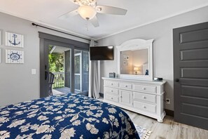 Une chambre à coucher avec un lit, une commode, un téléviseur et une porte.
