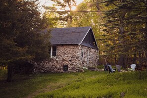 A stone cabin with a sloped roof surrounded by trees and grass. - Falcon Retreats - Pygmy (Sharbot Lake)