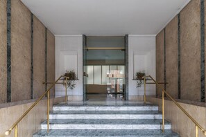 Eine Marmortreppe mit vergoldeten Handläufen führt zu einem Eingang mit Glastür.