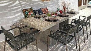 Ein Essbereich im Freien mit einem Steintisch, Korbstühlen und hängenden Rattanleuchten.