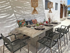 Ein Essbereich im Freien mit einem Steintisch, Korbstühlen und hängenden Rattanleuchten.
