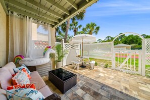 Eine überdachte Terrasse mit gepolsterten Sitzgelegenheiten, einem kleinen Tisch und einem Tiki-Sonnenschirm.