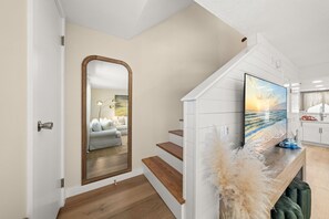 Ein modernes Interieur mit einer Holztreppe, einem großen Spiegel, einem Flachbildfernseher und einer Küchenzeile.