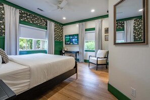Un dormitorio con una cama, un escritorio, una silla, un televisor y un espejo grande.