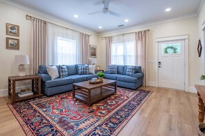Ein Wohnzimmer mit einem blauen Sofa, einem Couchtisch, einem gemusterten Teppich und einer Tür mit einer Milchglasverglasung.