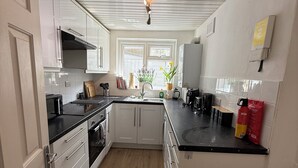 A kitchen with white cabinets, a black countertop, and a window with flowers. - Spacious 3 dbl bed house - sleeps 7! On the High St, 10 min walk to East Croydon (Croydon)