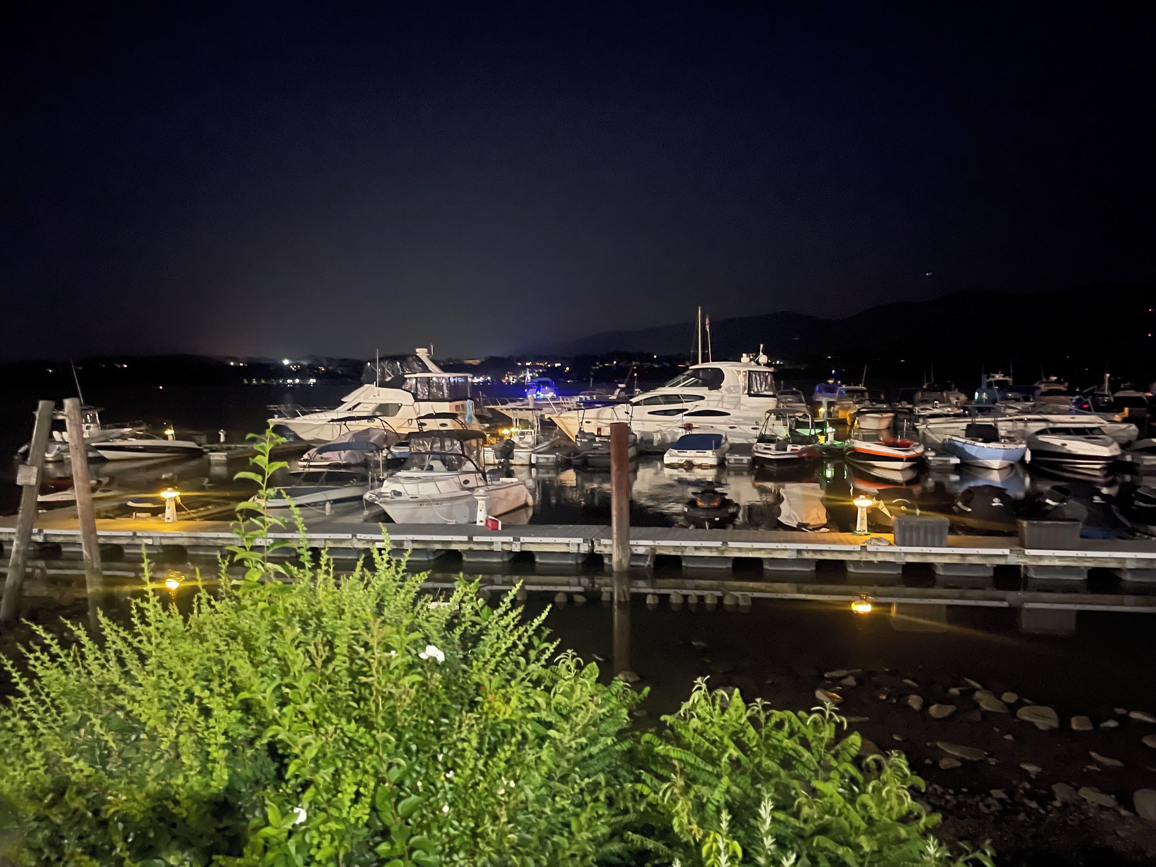 Un port de plaisance de nuit, avec des bateaux amarrés, un quai au premier plan et une montagne en arrière-plan.
