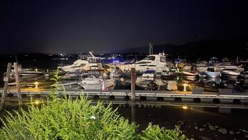 Un port de plaisance de nuit, avec des bateaux amarrés, un quai au premier plan et une montagne en arrière-plan.