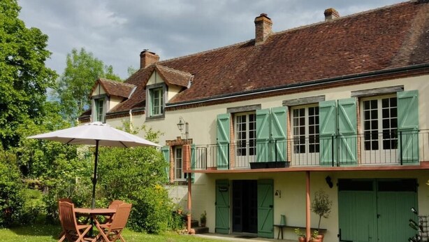 A two-story building with a balcony, a covered patio with outdoor furniture, and a well-maintained garden. - Bed & Breakfast Chez Mon Reve (Éguzon-Chantôme)