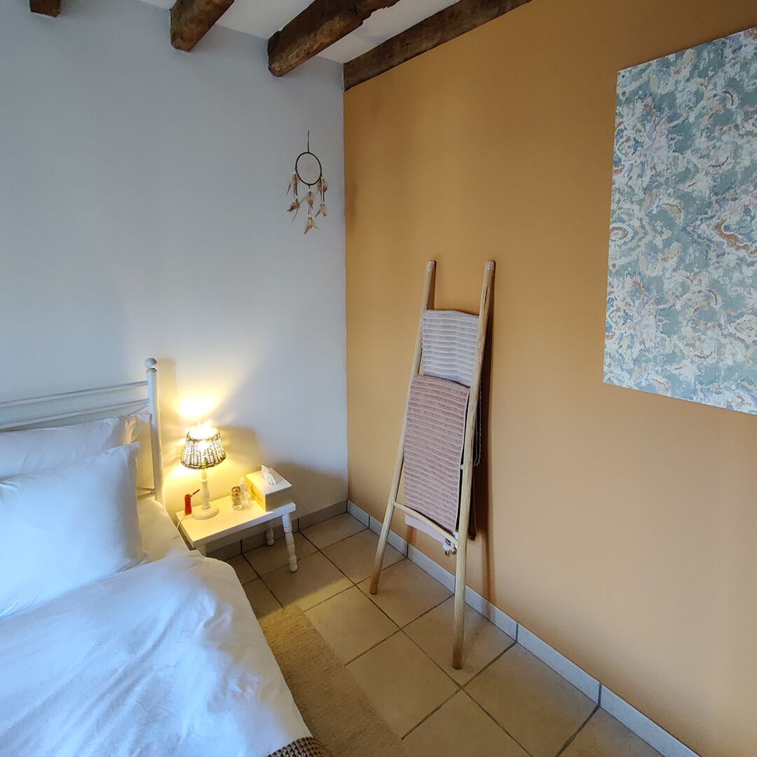 A bedroom with a bed, bedside table, lamp, and a wooden ladder leaning against the wall.