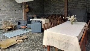 An outdoor patio with a table and chairs, a sofa, a TV, and a brick wall. - Bed & Breakfast Chez Mon Reve (Éguzon-Chantôme)