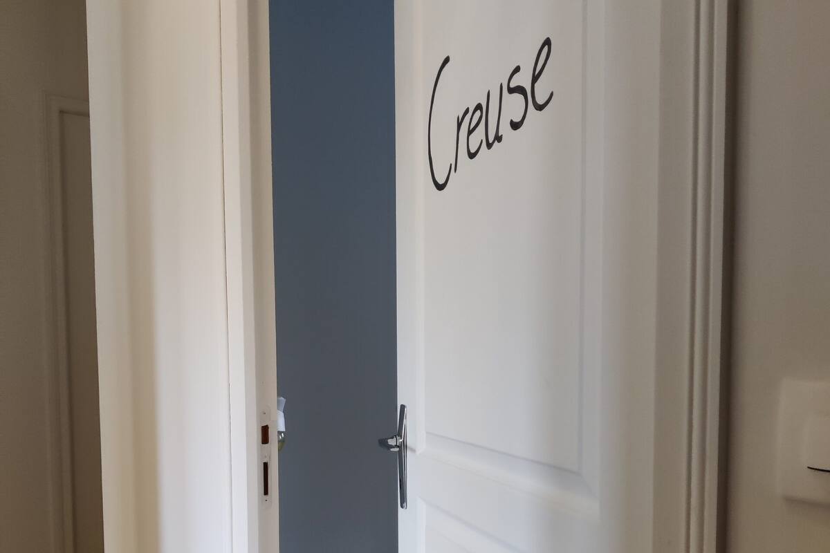 A white door with the word 'Creuse' on it, leading to a room with a wooden floor and a blue wall.