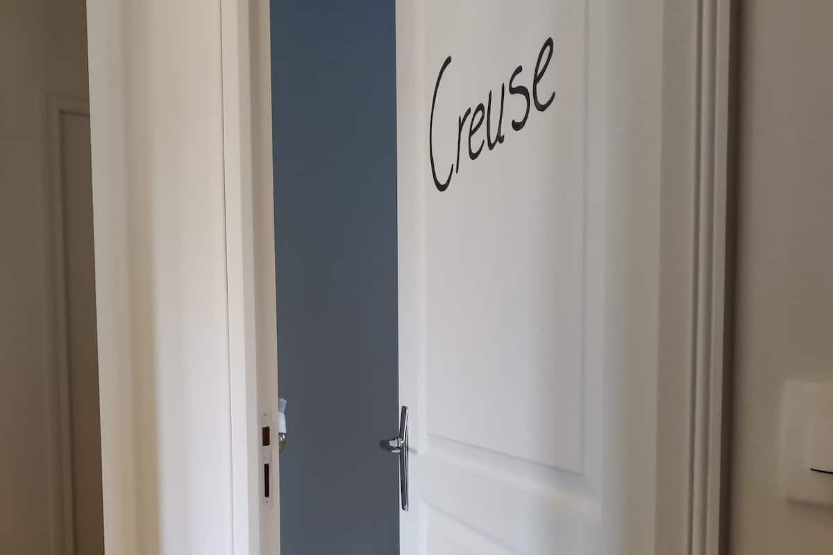A white door with the word 'Creuse' on it, leading to a room with a wooden floor and a blue wall.