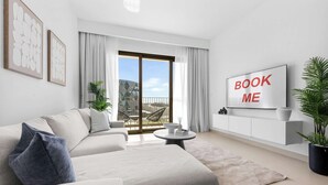 En moderne stue med sofa, sofabord, fjernsyn og en balkon med udsigt.