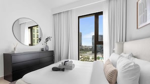 Et moderne hotelværelse med en stor seng, en sort kommode, et rundt spejl og udsigt over byen fra et stort vindue.