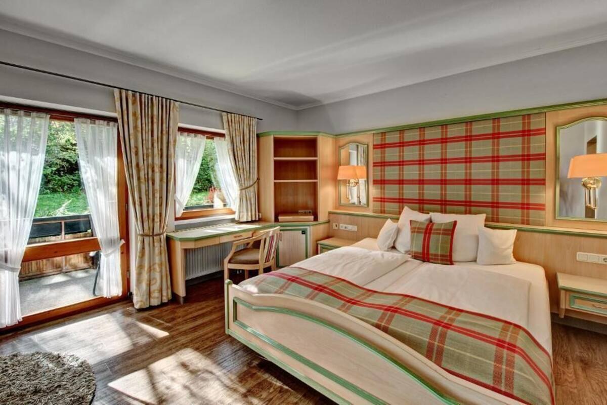 Ein Schlafzimmer mit Bett, Schreibtisch, Stuhl, Spiegel und einem Fenster mit Vorhängen.