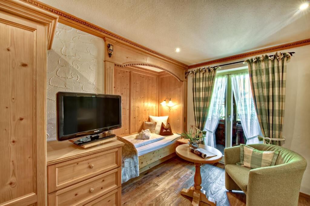 Ein gemütliches Zimmer mit einem Bett, einem Fernseher, einem Schreibtisch und einem Sessel.