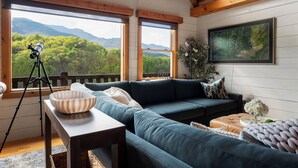 A cozy living room with a sectional sofa, a telescope on a tripod, and a painting of a forest. - Postcard-worthy views, 4 Decks, Jetted Tub (Burnsville)