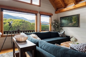 A cozy living room with a sectional sofa, a telescope on a tripod, and a painting of a forest.