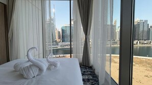 Ein Hotelzimmer mit Bett, durchsichtigen Vorhängen und Blick auf Stadtlandschaft und Strand.