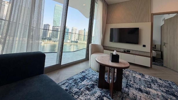 Ein modernes Hotelzimmer mit großem Fenster, Flachbildfernseher, Sofa, kleinem runden Tisch und Blick auf die Stadt.