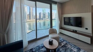 Ein modernes Wohnzimmer mit großem Fernseher, einer Couch, einem runden Couchtisch und Blick auf Stadt und Wasser.