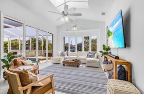 A spacious living area with a large window, ceiling fans, a flat-screen TV, and a pool view. - Peaceful Newly Renovated Canal Home in Punta Gorda (Punta Gorda)