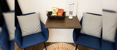 A room with two blue chairs, a small table with snacks, a WiFi sign, and a round rug with a central design.
