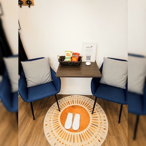 Huoneessa on kaksi sinistä tuolia, pieni pöytä, jossa on tarjolla pientä purtavaa, WiFi-merkki ja pyöreä matto, jonka keskellä on koristeellinen kuvio.