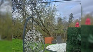 Um jardim com uma escultura metálica decorativa, um sequeiro e um guarda-chuva vermelho.