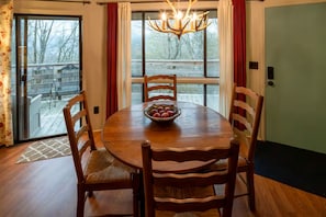 A dining area with a round wooden table, four wooden chairs, a chandelier, and a view through large windows. - Timber Ridge Sugar Mountain Condo. Sleeps 8. (Sugar Mountain)