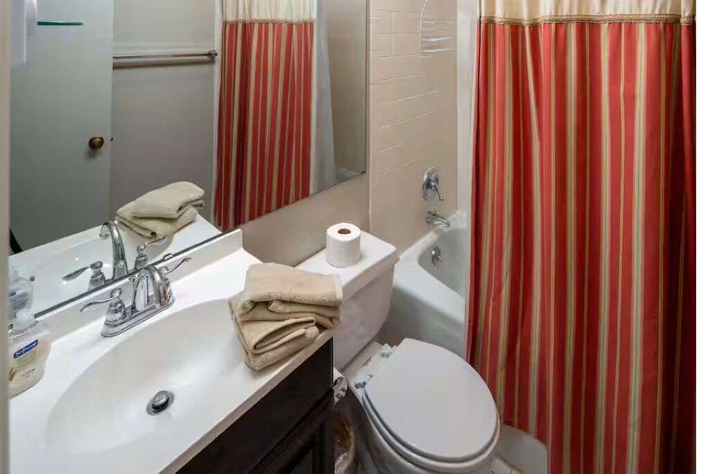 Un baño con lavamanos, espejo, inodoro y cortinas a rayas.