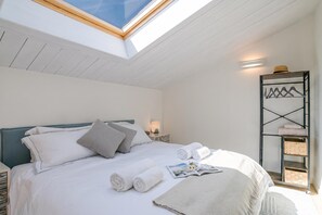 A bedroom with a skylight, a bed with pillows, rolled towels, a magazine, and a wall-mounted shelf with baskets. - Magical Menaggio Vista, Menaggio, Italy (Menaggio)