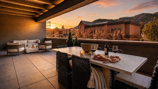 Eine Terrasse mit Esstisch, Gartenmöbeln und Blick auf Gebäude und Hügel.