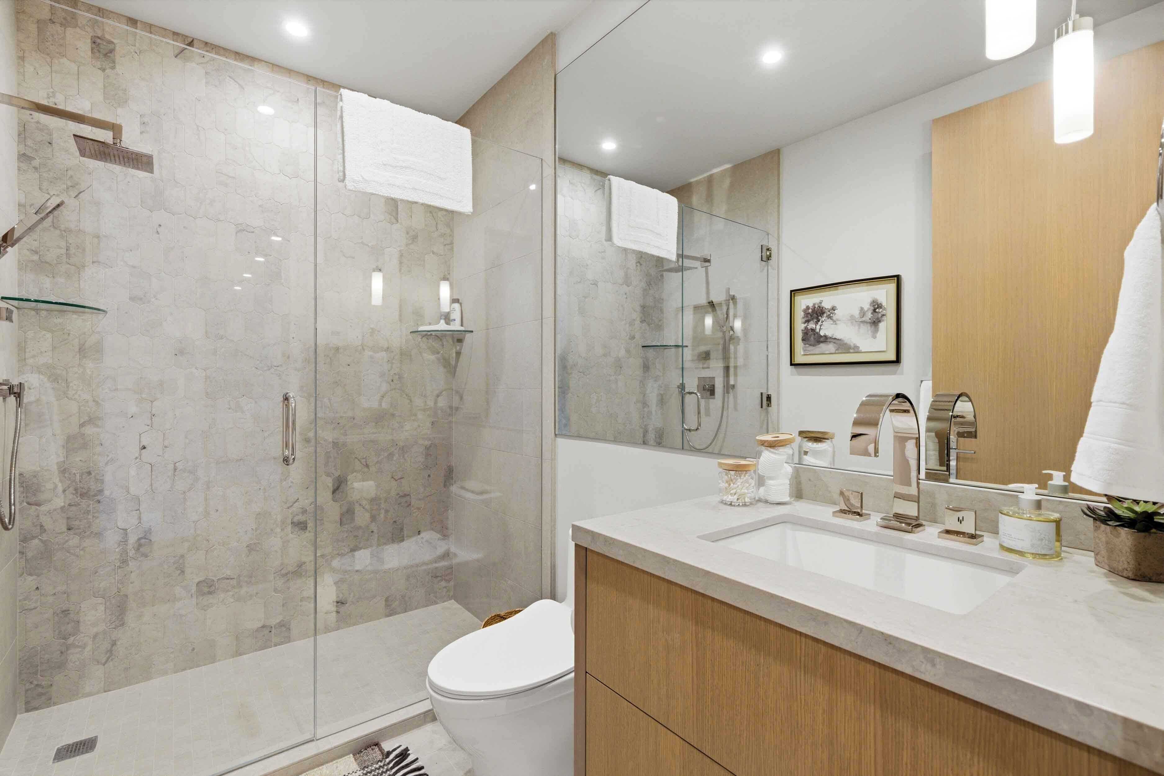A modern bathroom with a glass-enclosed shower, a white toilet, and a vanity with a large mirror.