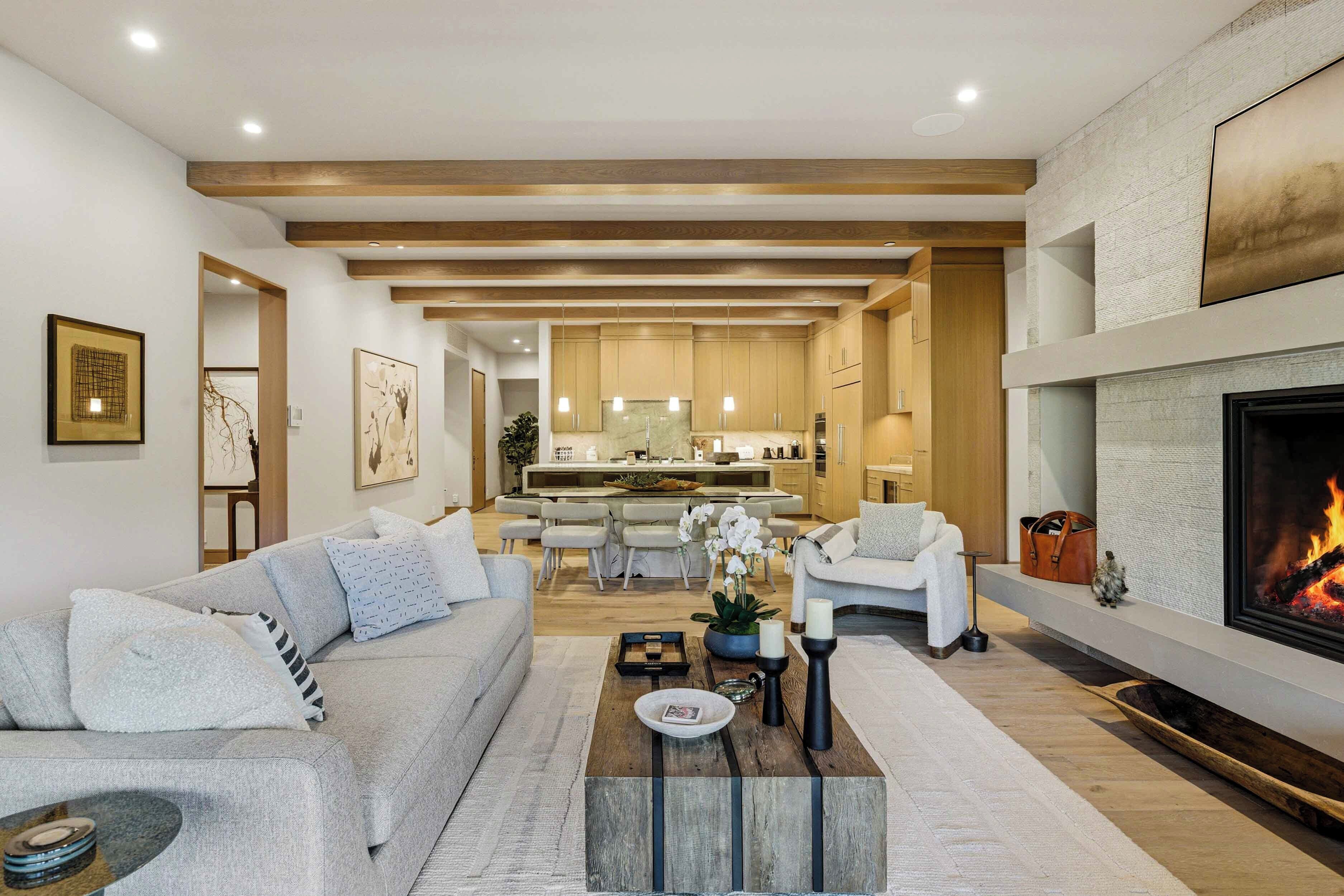 A modern living room with a sofa, coffee table, fireplace, and kitchen in the background.
