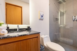 Ein Badezimmer mit einem Holzkosmetikschrank, einer Marmorarbeitsplatte, einer Toilette und einer Duschkabine.