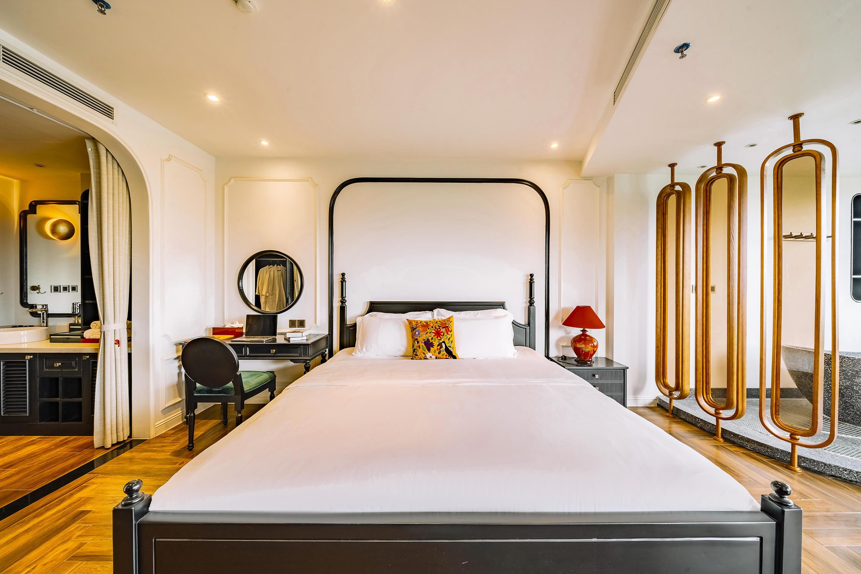 Una habitación de hotel moderna con una cama grande, un escritorio con una silla, un espejo y una lámpara roja.