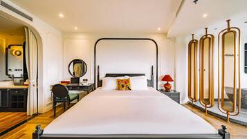 A modern hotel room with a large bed, a desk with a chair, a mirror, and a red lamp.