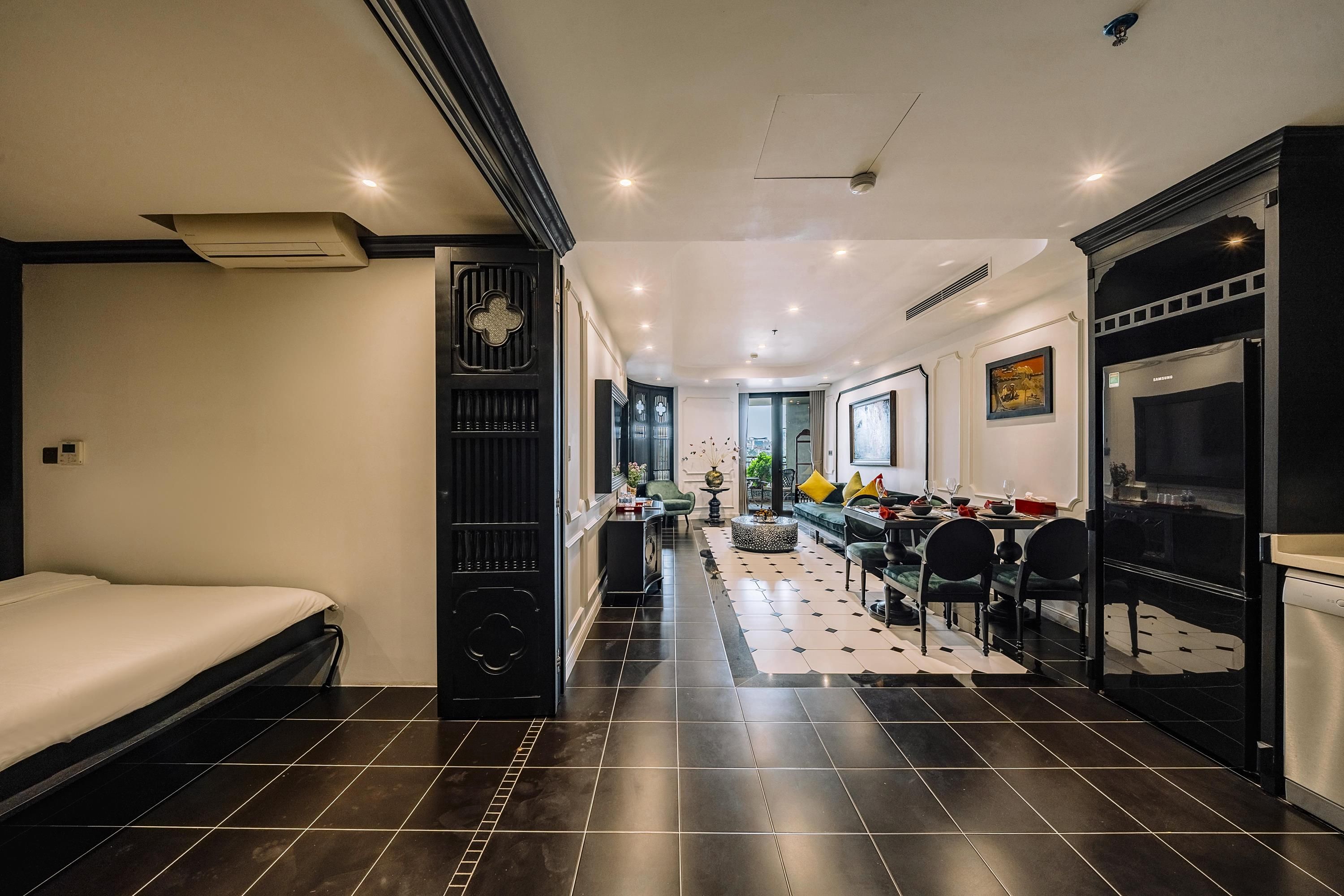 A modern hotel room with a bed, a dining area, and a kitchen.