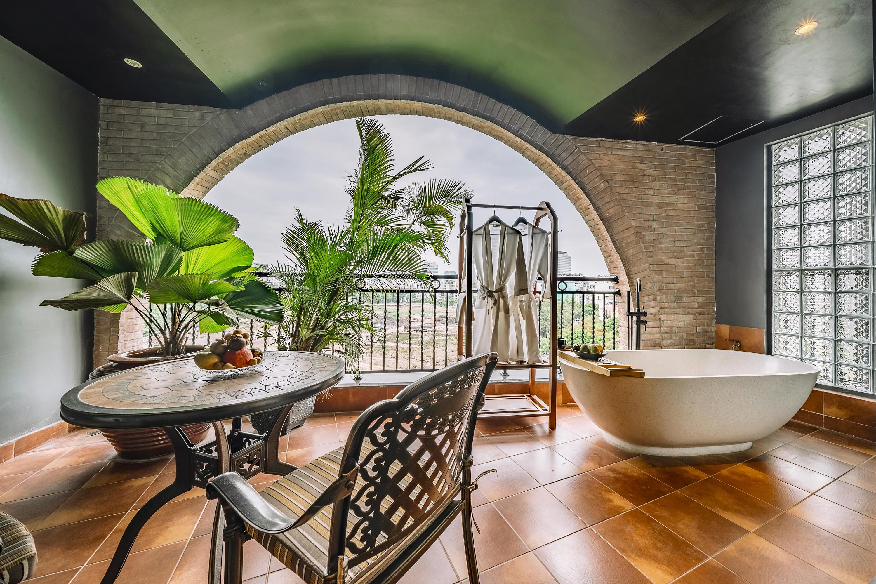 A modern bathroom with a freestanding bathtub, a round table with chairs, and a view through an arched window.