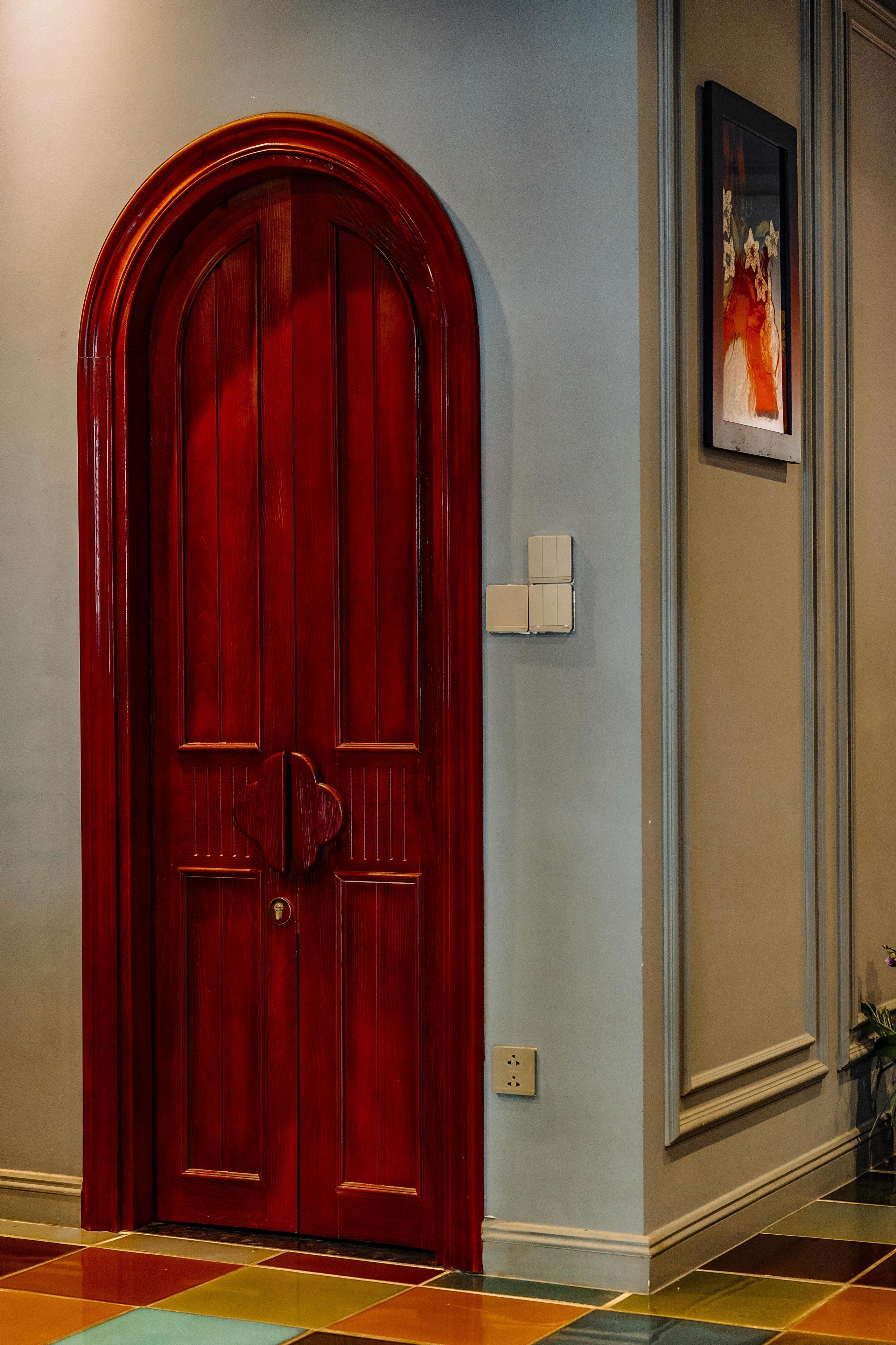A red door with a keyhole and a light switch on the wall beside it.