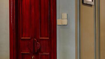 A red door with a keyhole and a light switch on the wall beside it.